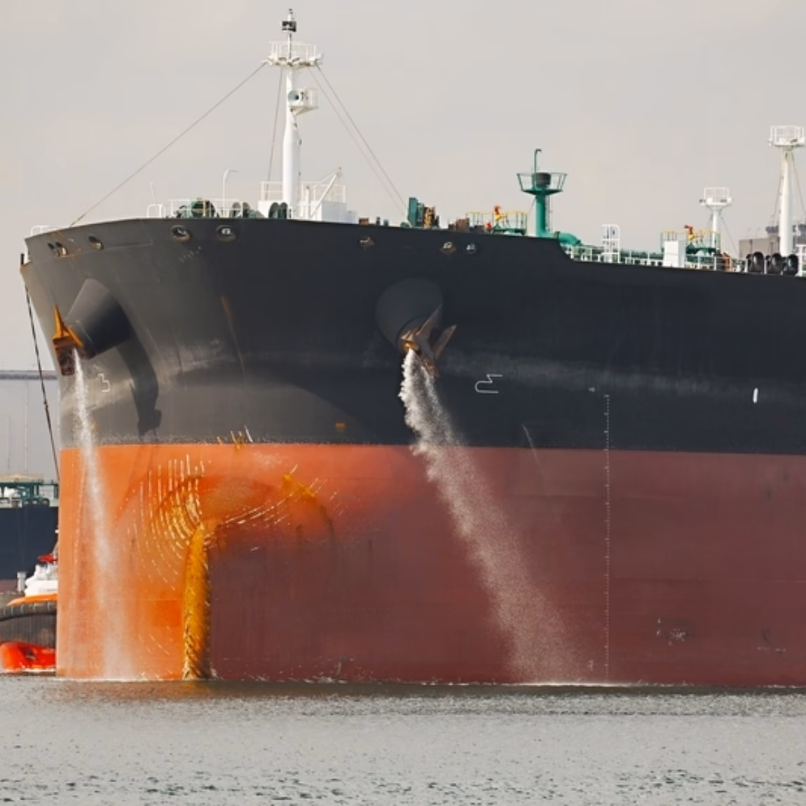 Tanker with water currents flowing past its bow in a harbor setting.