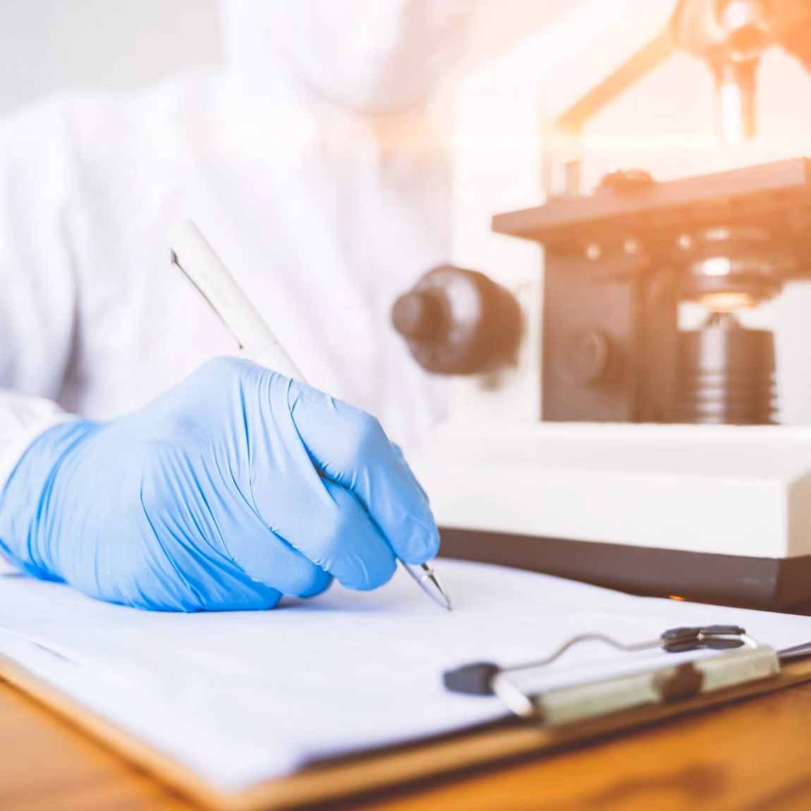 Ein Laborforscher mit blauem Handschuh arbeitet neben einem Mikroskop an der Analyse einer Probe.