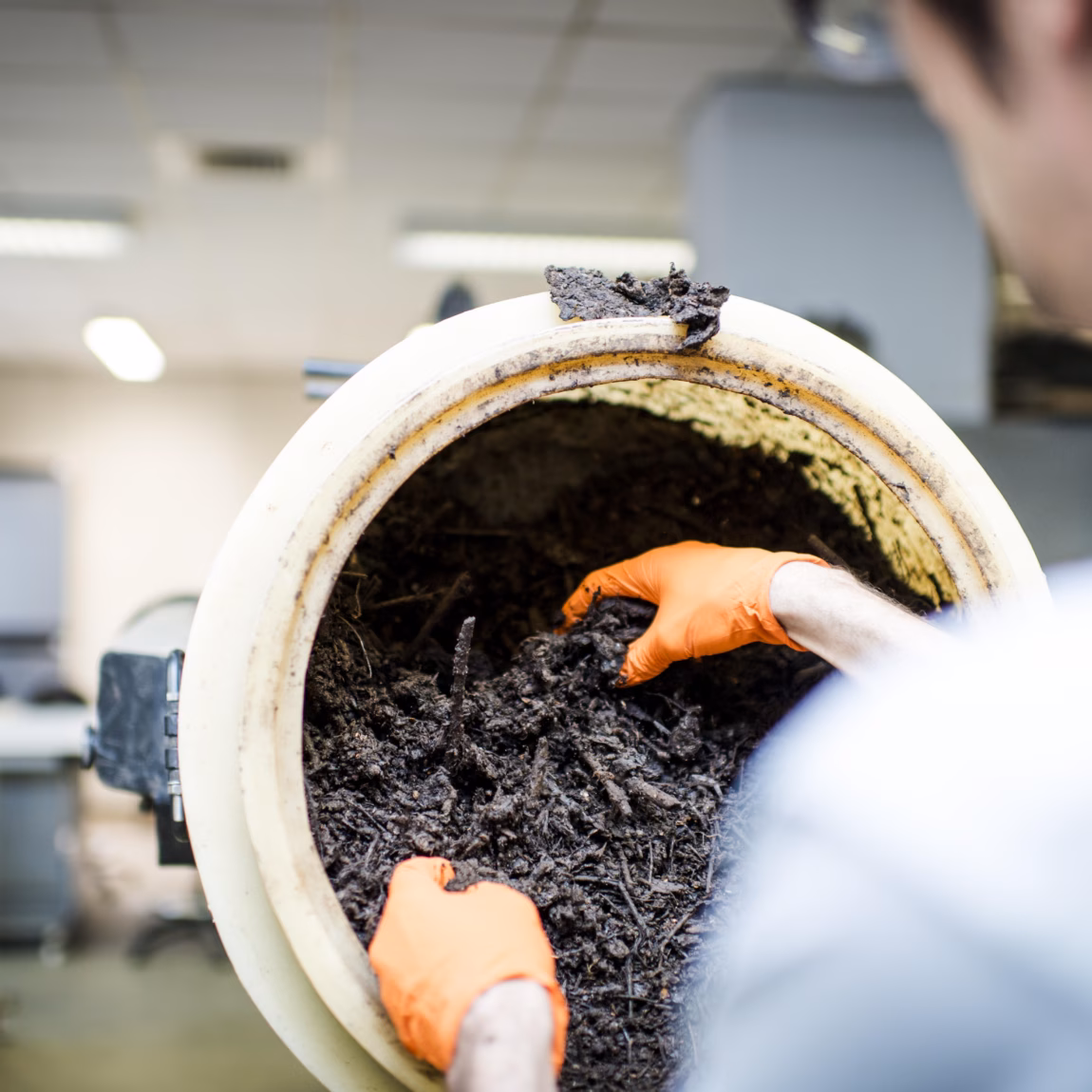 An employee examines a container of dark compost or soil samples in a laboratory setting.