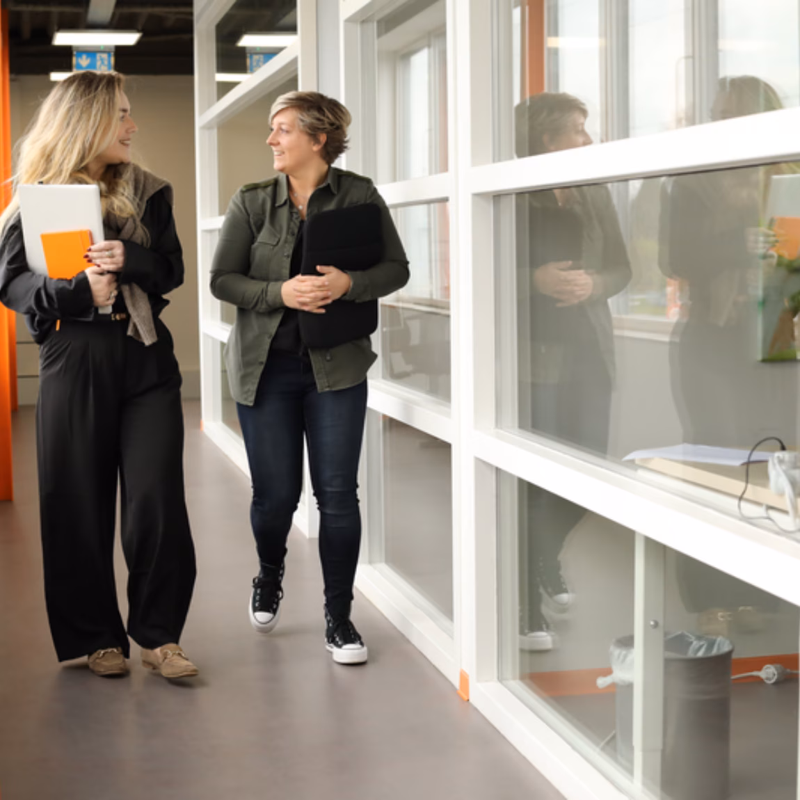 Twee medewerkers lopen door een kantooromgeving en bespreken werkzaamheden.