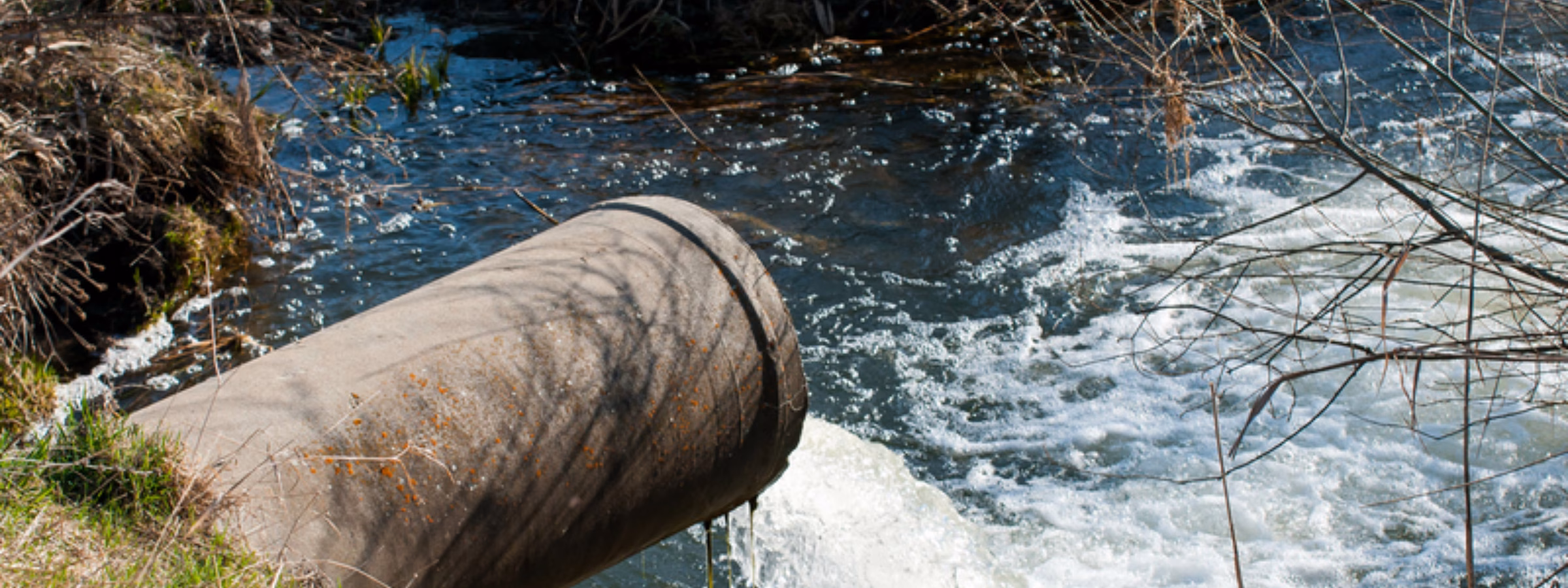 Afvoerbuis loost vervuild water in een beek of rivier langs een natuurlijke oever.
