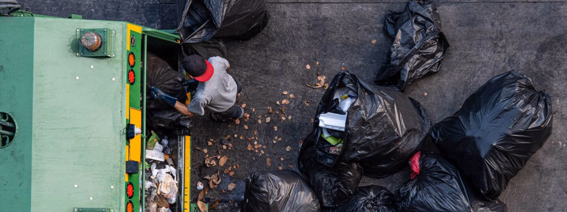 Véhicule de collecte des déchets entouré de sacs poubelles lors du traitement des déchets sur un terrain pavé.