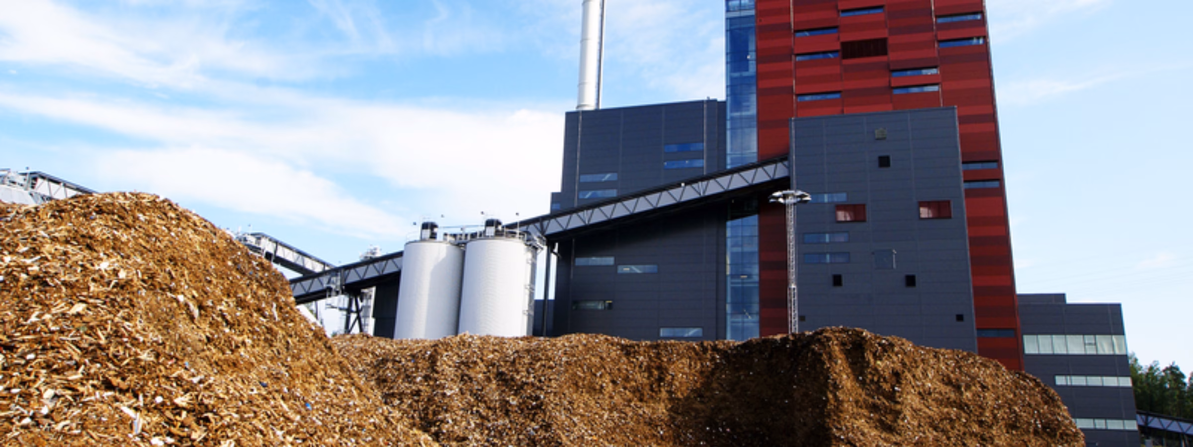 Biomassacentrale met grote hopen houtsnippers op een industrieterrein voor duurzame energieopwekking.