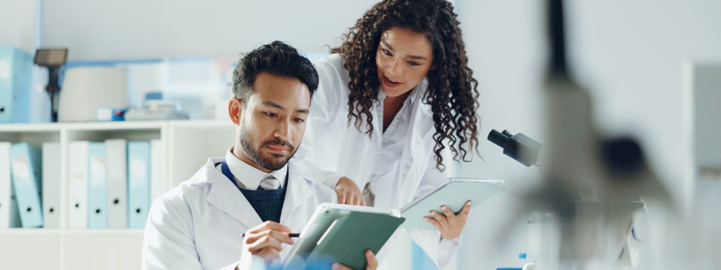 Twee laboratoriummedewerkers bekijken samen onderzoeksgegevens op een tablet in een moderne laboratoriumomgeving.
