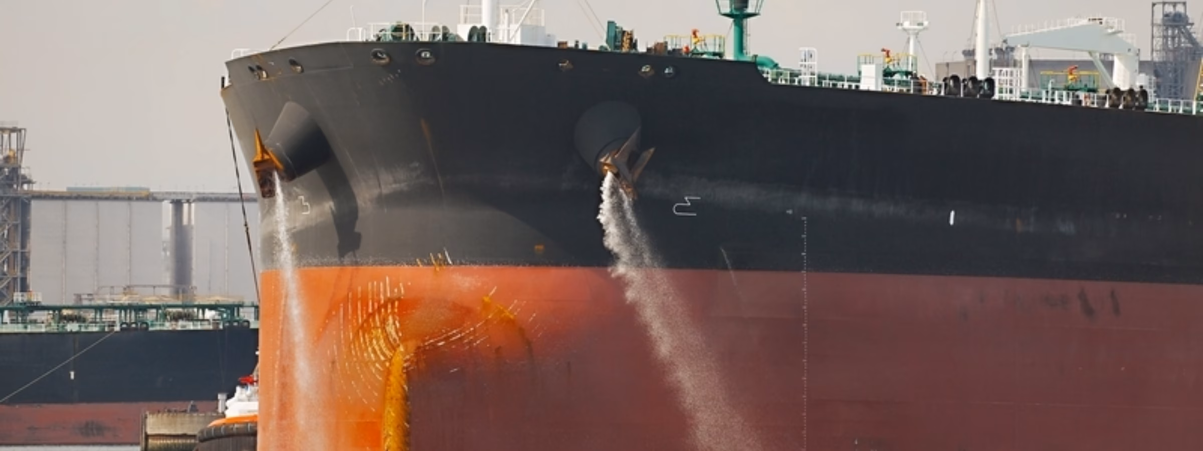 Tanker with water currents flowing past its bow in a harbor setting.