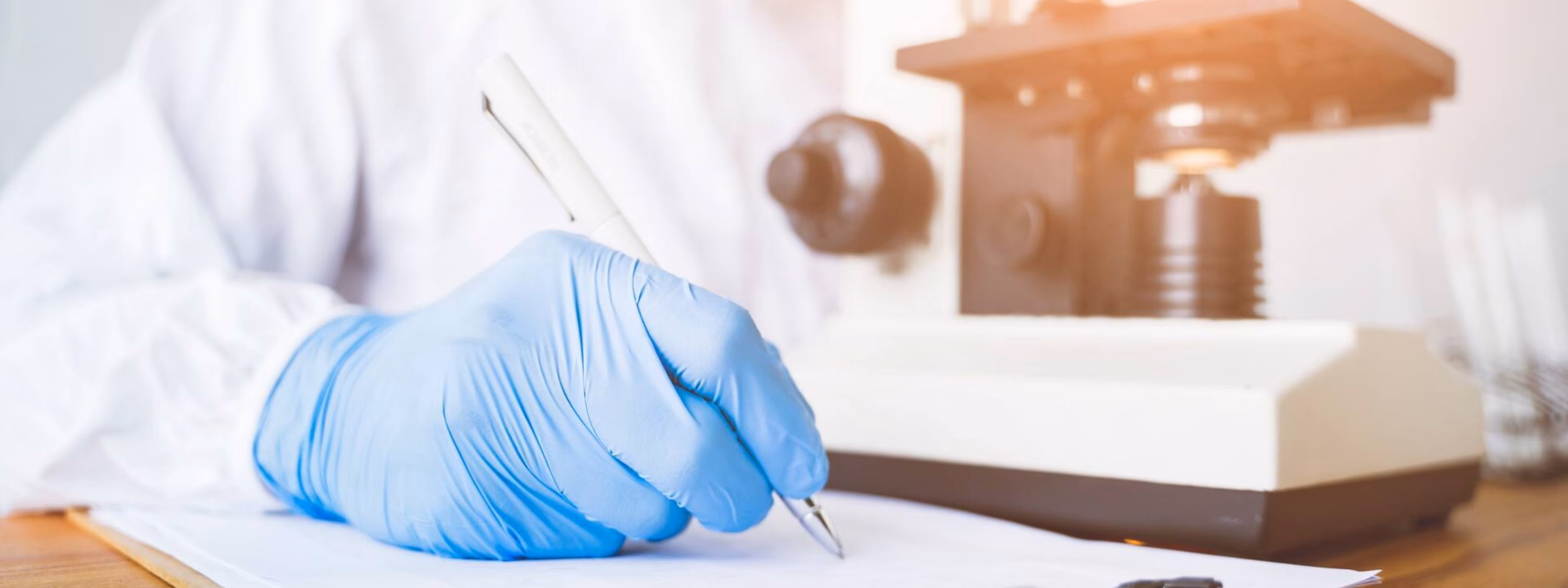 Ein Laborforscher mit blauem Handschuh arbeitet neben einem Mikroskop an der Analyse einer Probe.