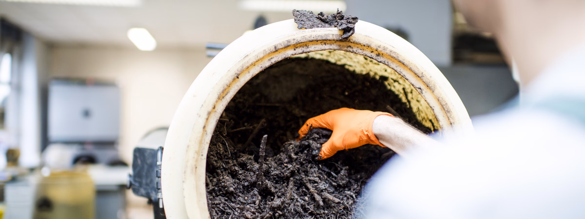 An employee examines a container of dark compost or soil samples in a laboratory setting.