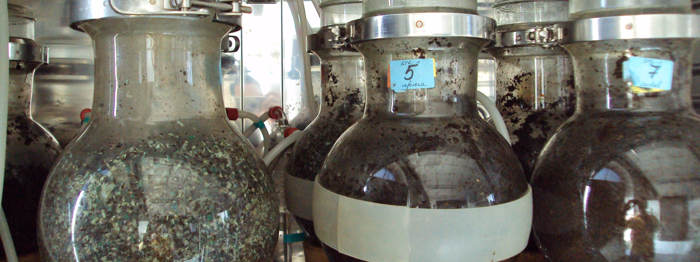 Industrial glass fermentation tanks containing a dark liquid in a production facility.