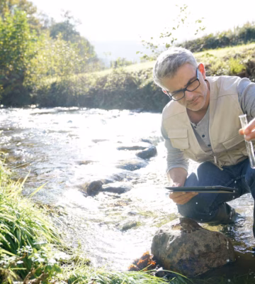 Medewerker neemt een watermonster uit een stromende rivier voor onderzoek naar de waterkwaliteit.