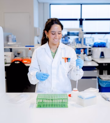 Laboratoriummedewerker in een witte labjas en blauwe handschoenen onderzoekt monsters met een pipet in een laboratorium.