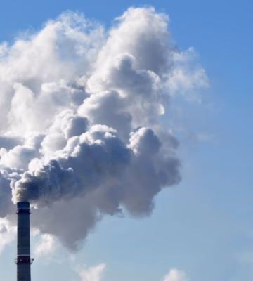 Les cheminées d'une installation industrielle rejettent des gaz de combustion dans un ciel bleu limpide.
