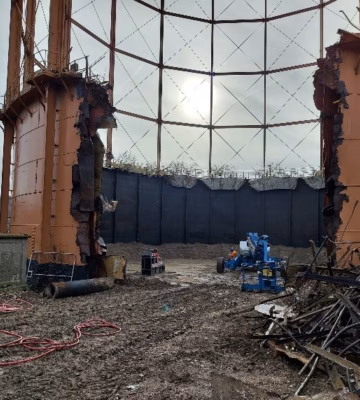 Binnenzijde van een grote industriële opslagtank met metalen constructies, leidingen en werkzaamheden op de bodem.