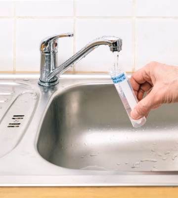 Medewerker houdt een monsterbuisje onder een kraan boven een gootsteen om een drinkwatermonster te nemen.