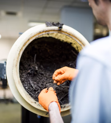Une personne examine un échantillon organique foncé dans un tambour rotatif de laboratoire.