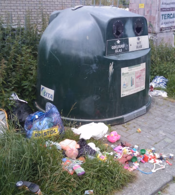 Des déchets sauvages jonchent le sol autour d’un conteneur à verre, ce qui témoigne d’une pollution au niveau d’un point de collecte.
