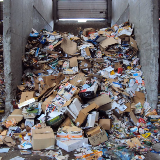 Gemengd afval en karton op een sorteer- of overslaglocatie voor afvalverwerking.