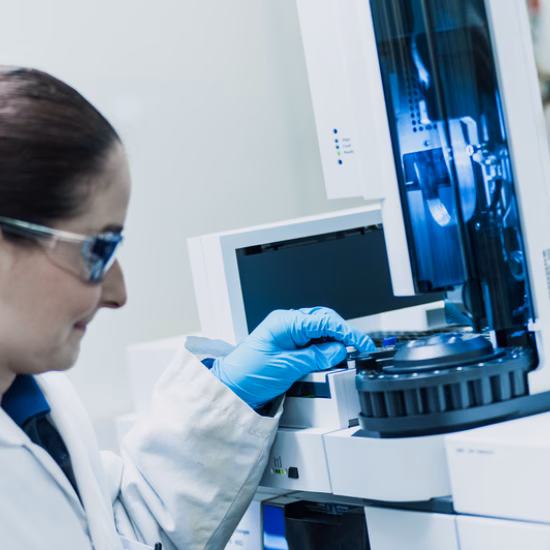 Laboratoriummedewerker met handschoenen plaatst een monster in een analytisch laboratoriuminstrument.