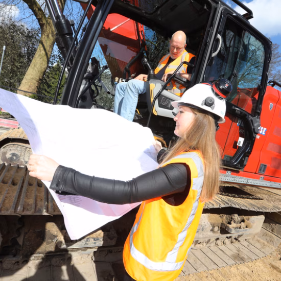 Een bouwtekening wordt geraadpleegd tijdens werkzaamheden op een bouwplaats met graafmachine.