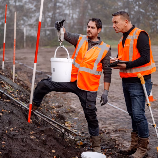 Medewerkers nemen een grondmonster en registreren meetgegevens voor bodemonderzoek.
