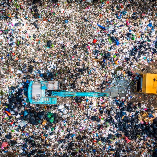Luchtfoto van een afvalverwerkingslocatie met voertuigen en grote hoeveelheden gemengd afval.