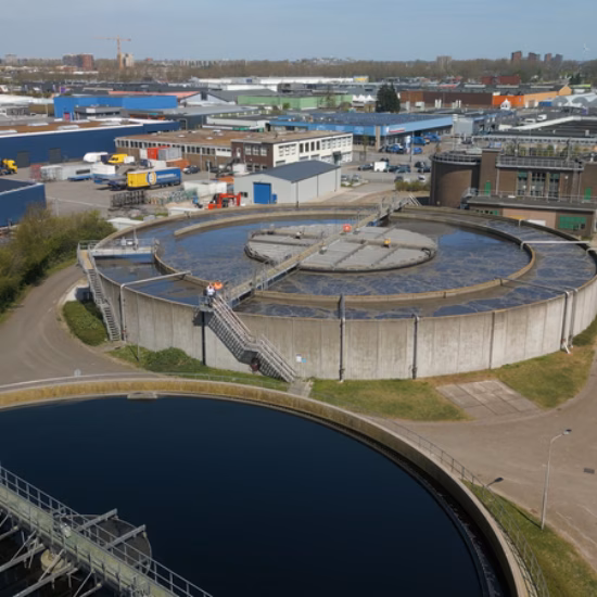 Luchtfoto van een waterzuiveringsinstallatie met verschillende bassins en zuiveringsprocessen.
