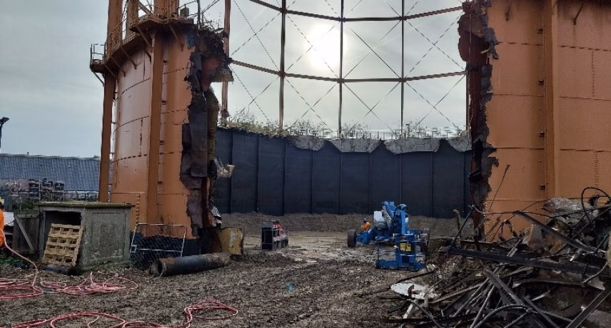 Binnenzijde van een grote industriële opslagtank met metalen constructies, leidingen en werkzaamheden op de bodem.