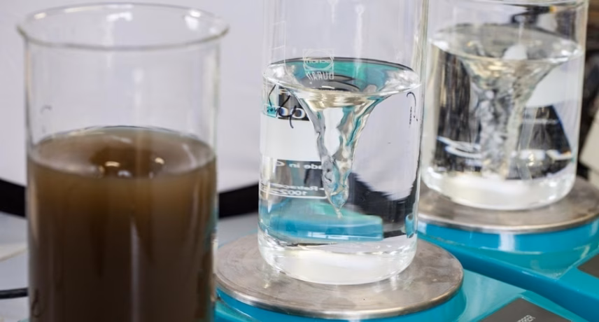 Trois béchers en verre posés sur une balance de laboratoire lors d'une mesure de la qualité de l'eau. Le bécher de gauche contient de l'eau brune et trouble, tandis que ceux du milieu et de droite contiennent de l'eau claire.