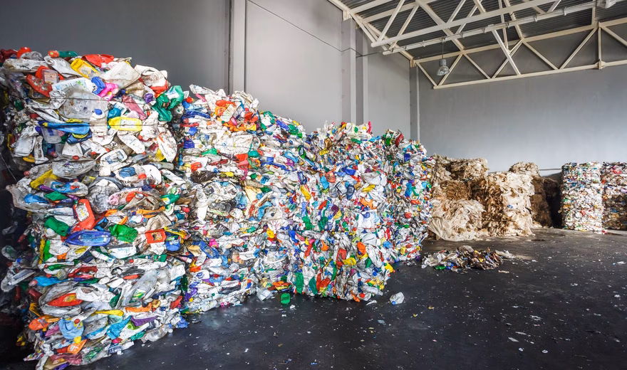 Samengeperste balen kunststof- en verpakkingsafval opgeslagen in een recyclinghal voor afvalverwerking.