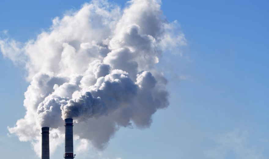 Schoorstenen van een industriële installatie stoten rookgassen uit tegen een heldere blauwe lucht.
