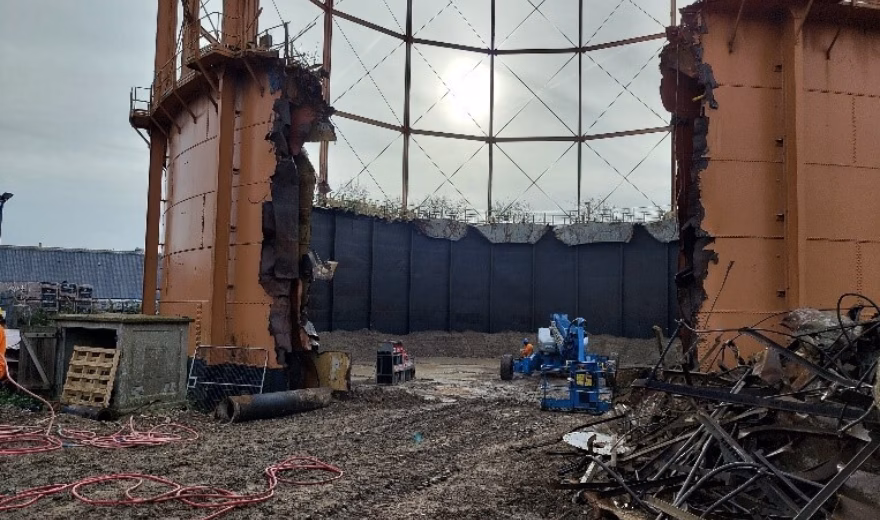 Binnenzijde van een grote industriële opslagtank met metalen constructies, leidingen en werkzaamheden op de bodem.
