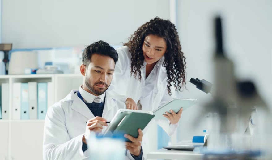 Twee laboratoriummedewerkers bekijken samen onderzoeksgegevens op een tablet in een moderne laboratoriumomgeving.
