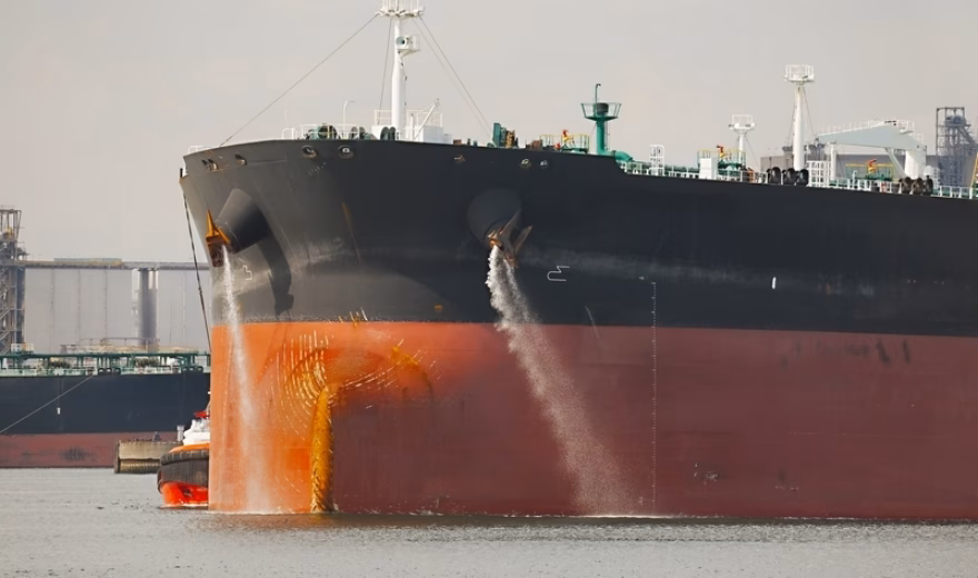 Tanker with water currents flowing past its bow in a harbor setting.
