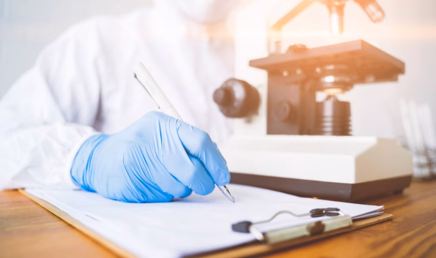 A laboratory researcher wearing a blue glove works on sample analysis next to a microscope.
