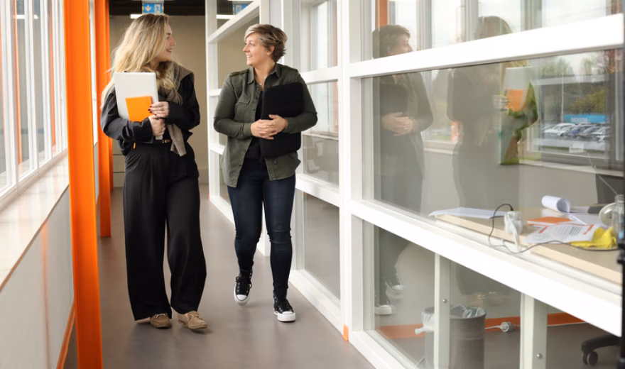 Twee medewerkers lopen door een kantooromgeving en bespreken werkzaamheden.