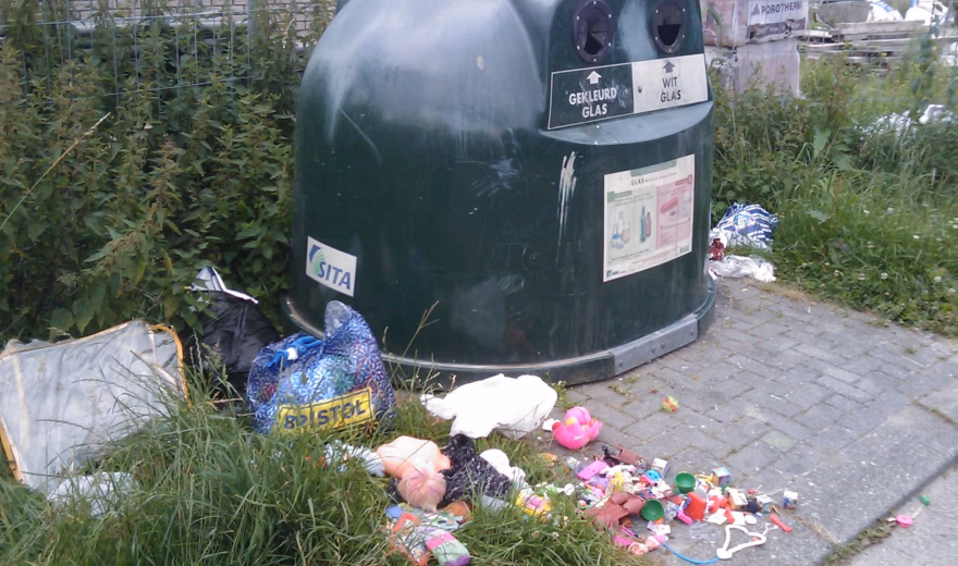 Rond een glascontainer ligt zwerfafval, wat wijst op vervuiling bij een inzamelpunt.