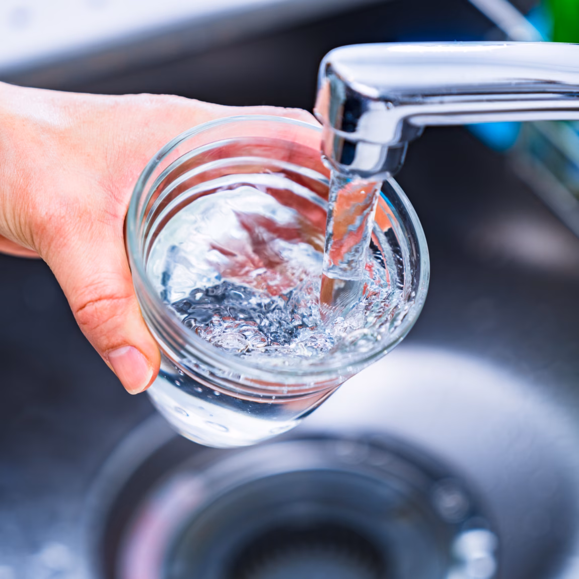 Watermonster wordt afgenomen uit een kraan in een glazen pot voor wateronderzoek.