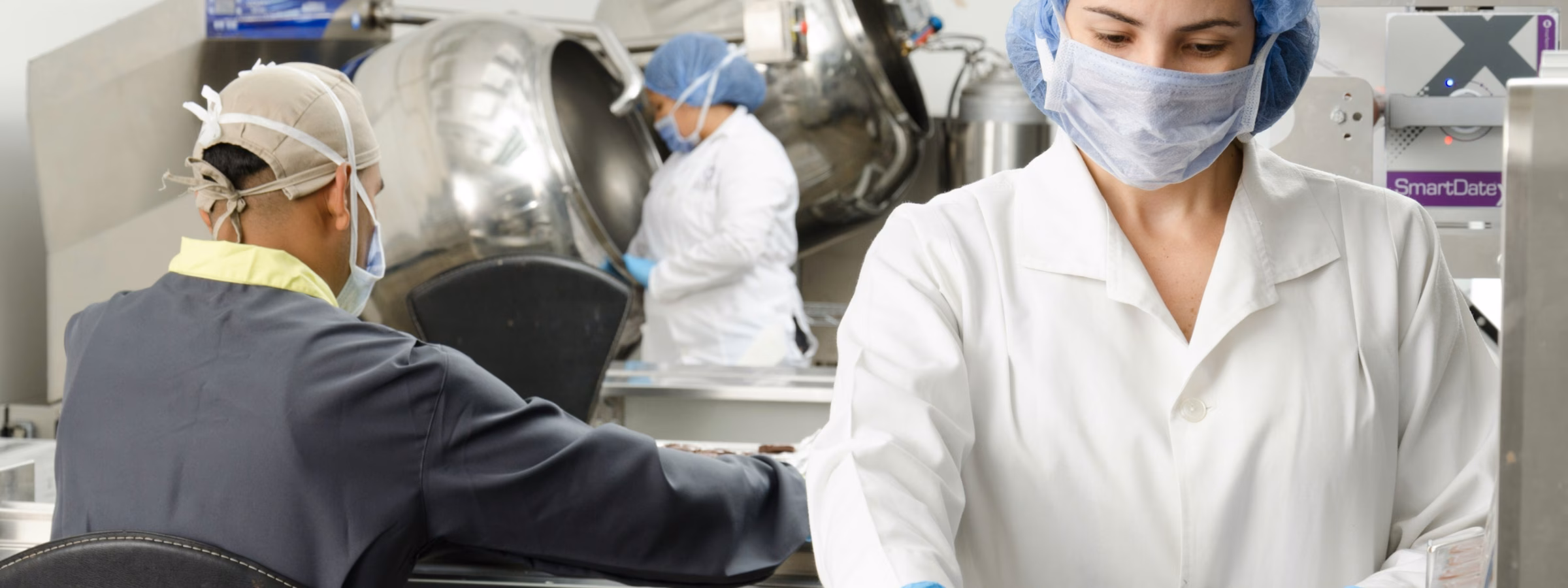 Employees perform visual inspections of food products in a production environment.