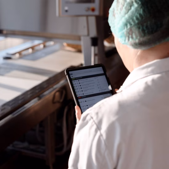 Medewerker in hygiënische werkkleding gebruikt een tablet voor digitale kwaliteitscontrole in een productieomgeving.