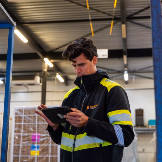 Medewerker in veiligheidskleding controleert logistieke processen in een magazijn met behulp van een tablet.