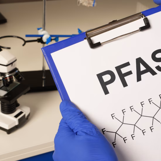 Laboratoriummedewerker houdt een klembord met PFAS vast naast laboratoriumapparatuur.