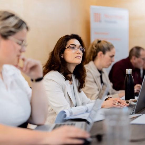 Participants in a business training session or meeting are working on laptops at a conference table.