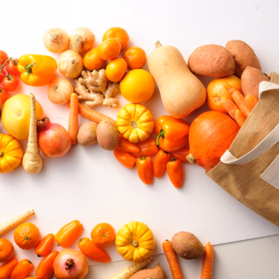 Herfstgroenten en fruit naast een herbruikbare boodschappentas op een lichte achtergrond.