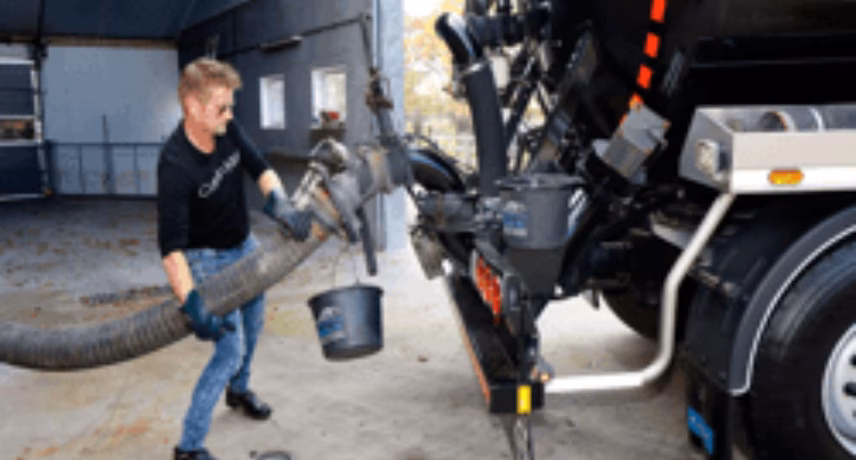 Medewerker koppelt een grote afzuigslang aan een industriële vacuümwagen voor het leegzuigen van materiaal.