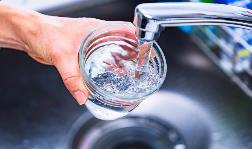 Watermonster wordt afgenomen uit een kraan in een glazen pot voor wateronderzoek.