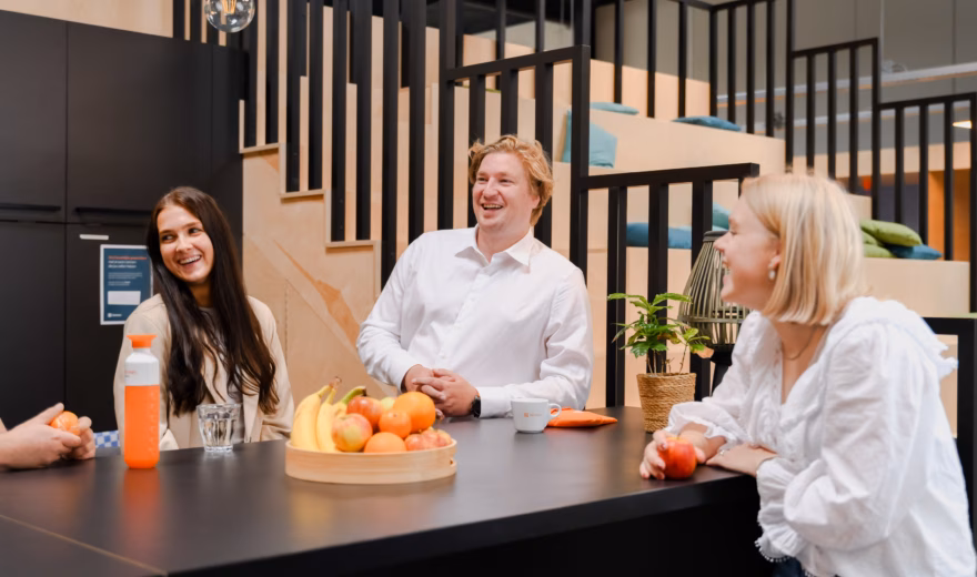 Colleagues are sitting together at a table in an office space during a casual break.