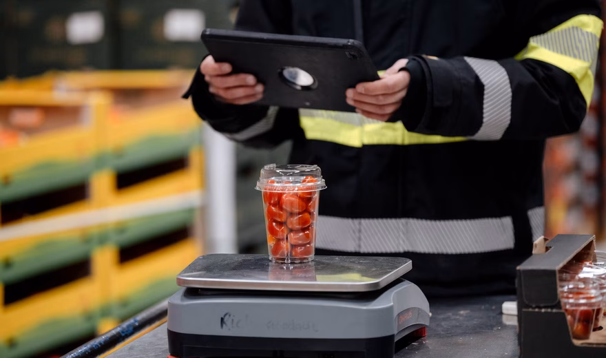 Magazijnmedewerker gebruikt een tablet naast een industriële weegschaal met verpakte producten tijdens logistieke controle.