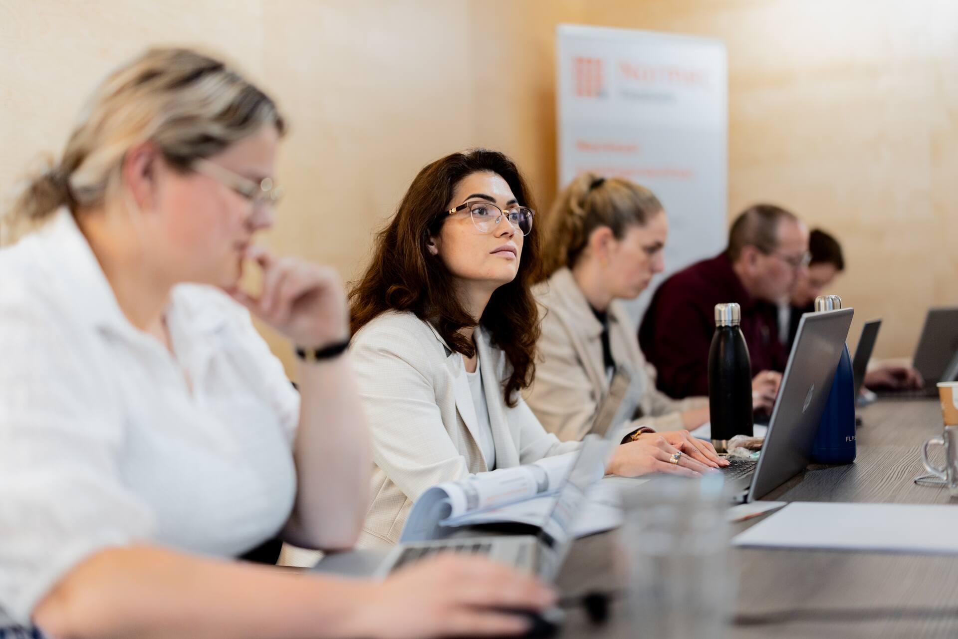 Teilnehmer einer geschäftlichen Schulung oder Veranstaltung arbeiten mit Laptops an einem Konferenztisch.