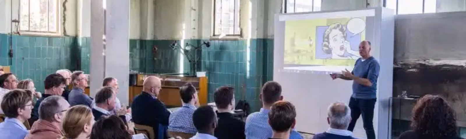 Een spreker geeft een presentatie aan een groep deelnemers tijdens een bijeenkomst of training.