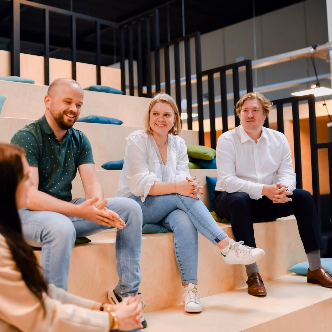 A group discussion among four professionals in a modern office setting with wooden bleacher seating.