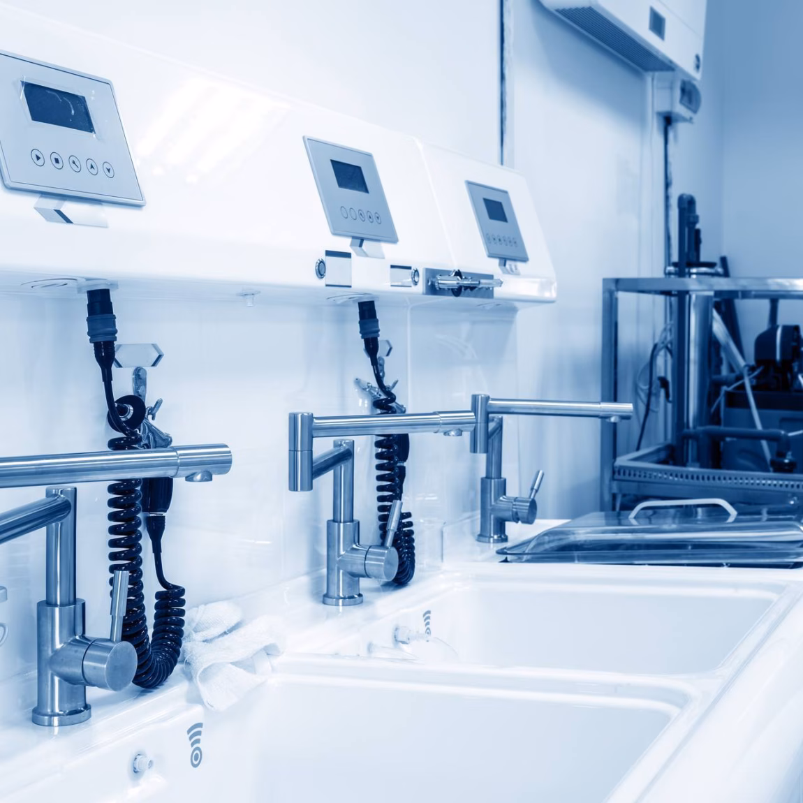 Steriele wasruimte met medische wastafels, dispensers en monitoringapparatuur voor hygiëne in een zorgomgeving.